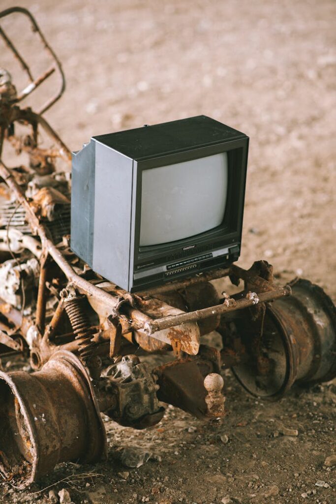A vintage TV set sits on rusty, abandoned machinery outdoors, capturing nostalgia and decay.